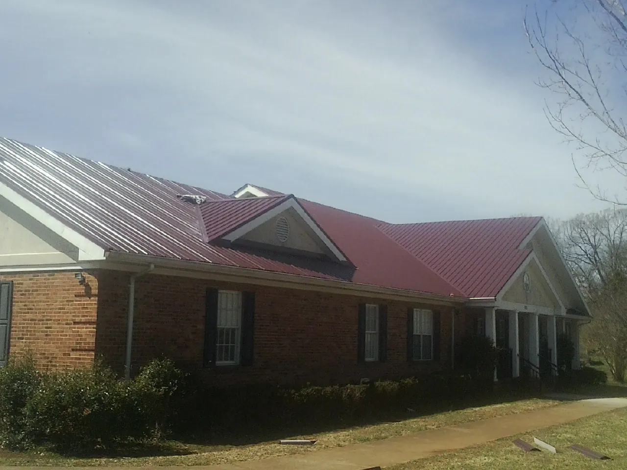 Red metal roof with gabled entries on a long brick building, from a Hail Damage Roof Repair job in Tyaskin