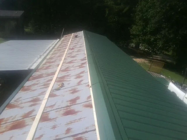 Old rusted panels beside newly installed green metal roofing — Wind Damage Roof Repair by Roofing Brothers in Tyaskin