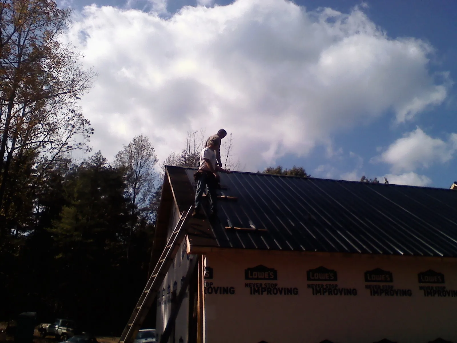 Roofer fastening dark metal panels high against a cloudy sky, from a Roof Inspection job in Tyaskin