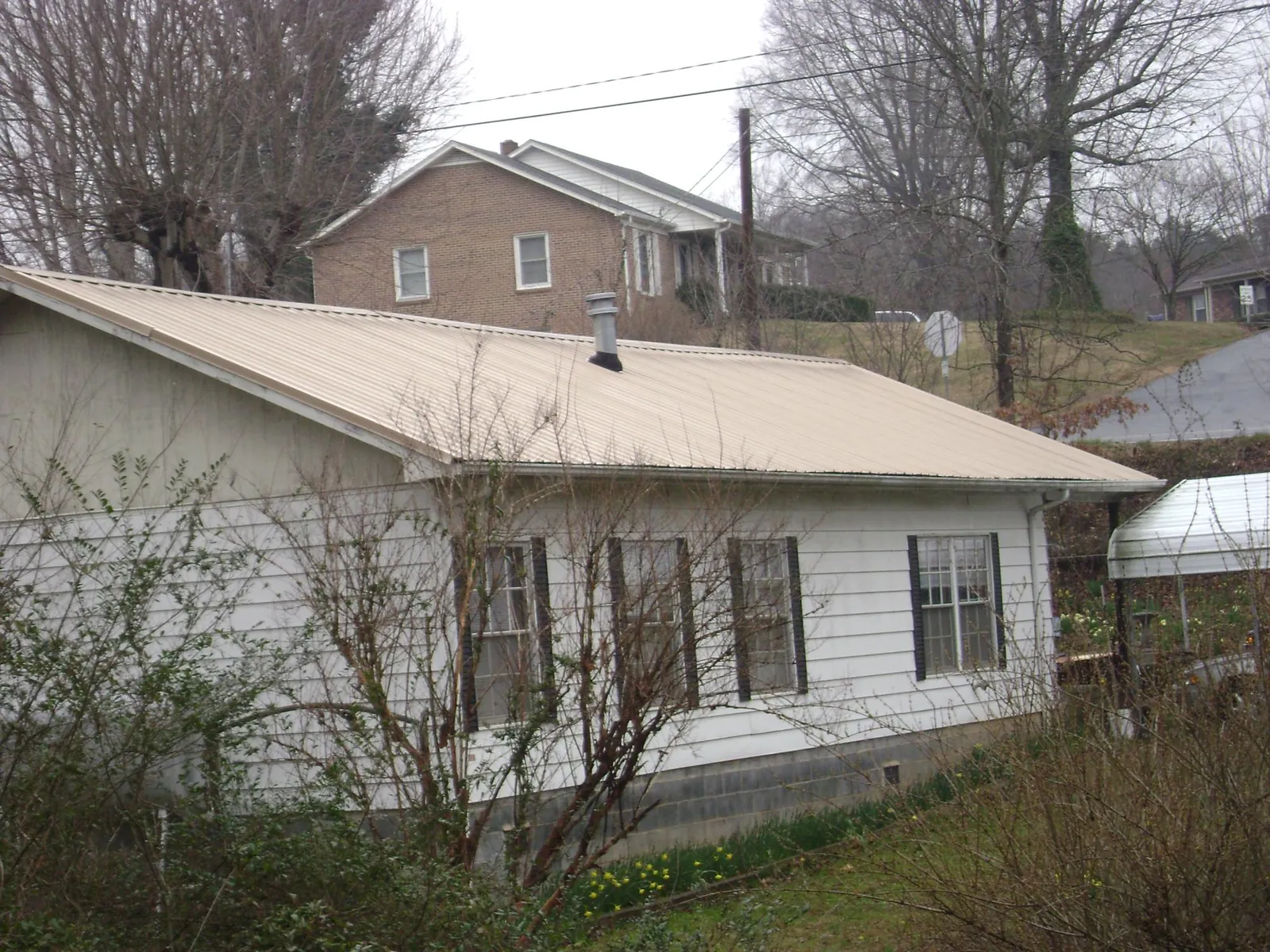 Tan metal roof on a white sided house set into a hillside — Commercial Roofing by Roofing Brothers in Tyaskin